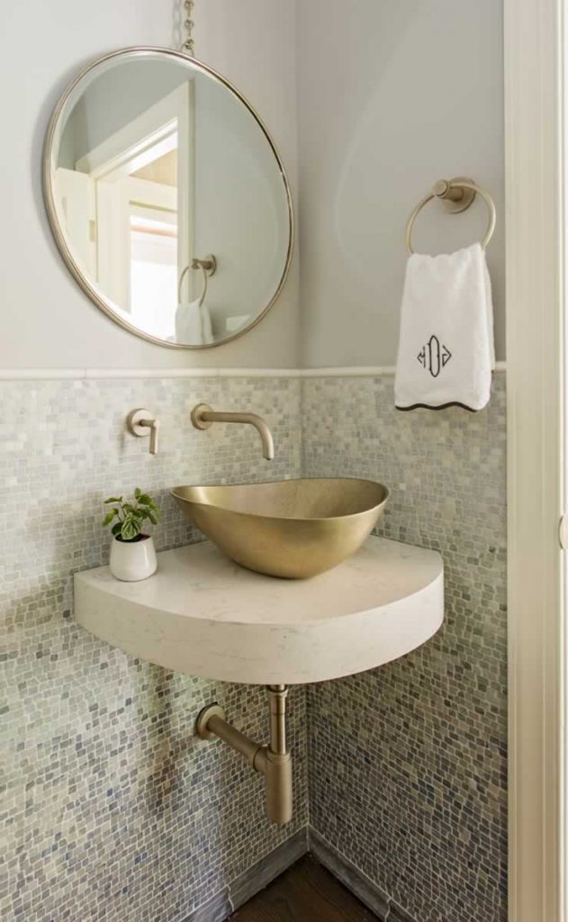 powder room with blue ombre mosaic tile, gold vessel sink on wall-mounted platform, and round mirror